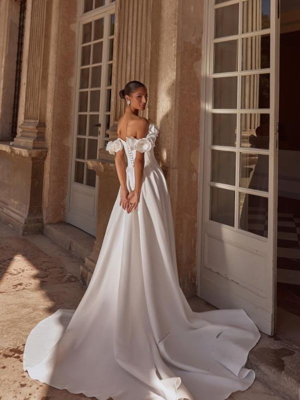 Χολιβουντιανό νυφικό από σατέν με ανοιχτούς ώμους με τρισδιάστατα λουλούδια.